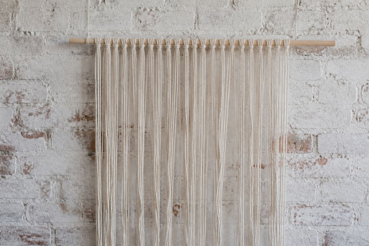 Loose undyed cotton cords hanging from a wooden dowel before knotting