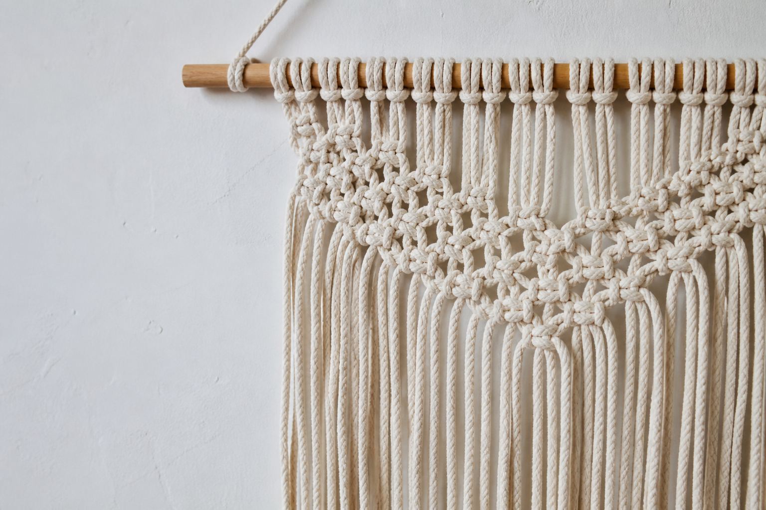 Cream cotton macramé wall hanging with square knots and fringe on a chalk studio wall